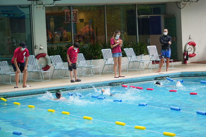 海外学生会成员为参加慈善游泳比赛的参赛者计时，纪录完成时间